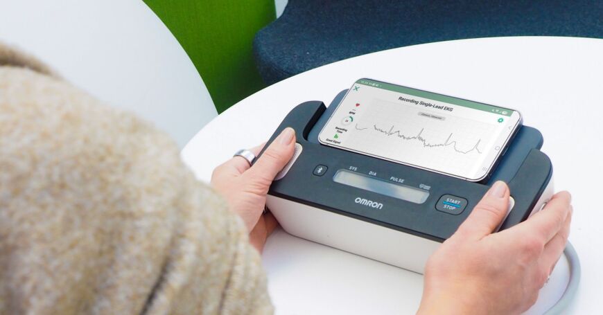 Nainen mittaa EKG:n Omron Complete -mittarilla. 