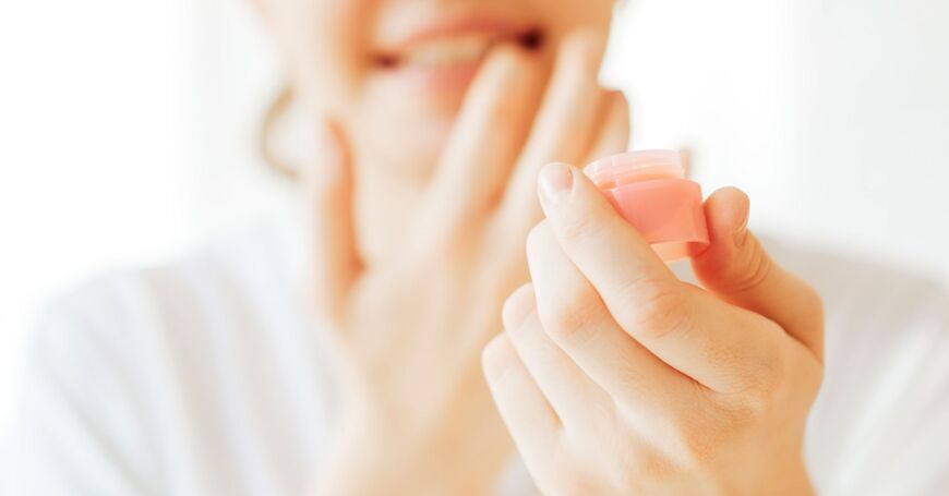Naisen rohtuneet huulet paranevat, kun hän levittää huulilleen apteekin huulivoidetta.