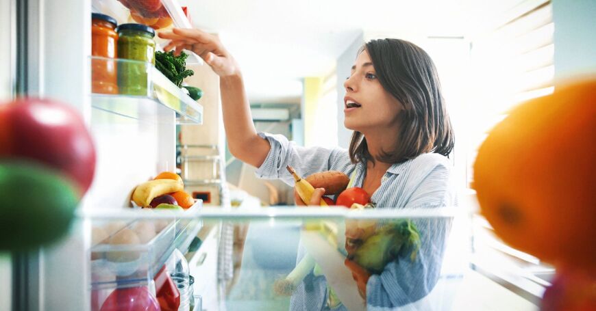 Nainen ottaa jääkaapista B-vitamiinia sisältäviä hedelmiä ja vihanneksia