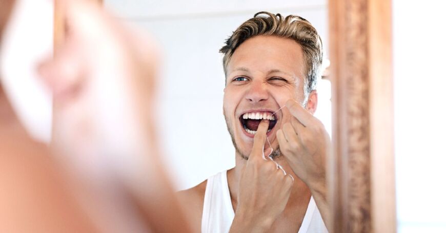 Nuori mies käyttää hammaslankaa peilin edessä