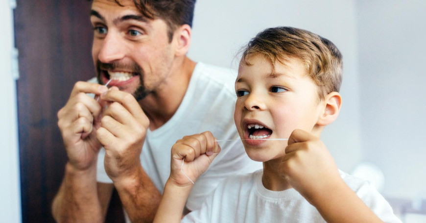 Isä opastaa pojalleen hammaslangan käyttöä kylpyhuoneessa.