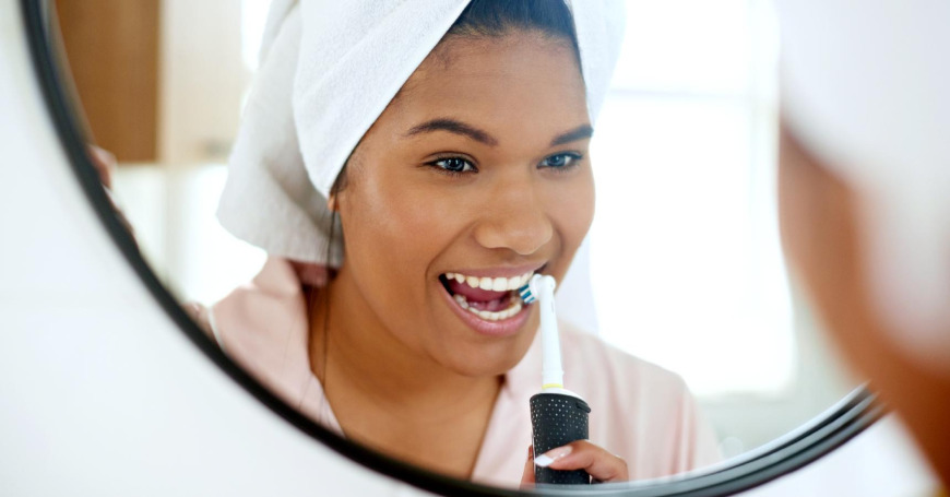Nainen pesee peilin edessä hampaitaan sähköhammasharjalla.